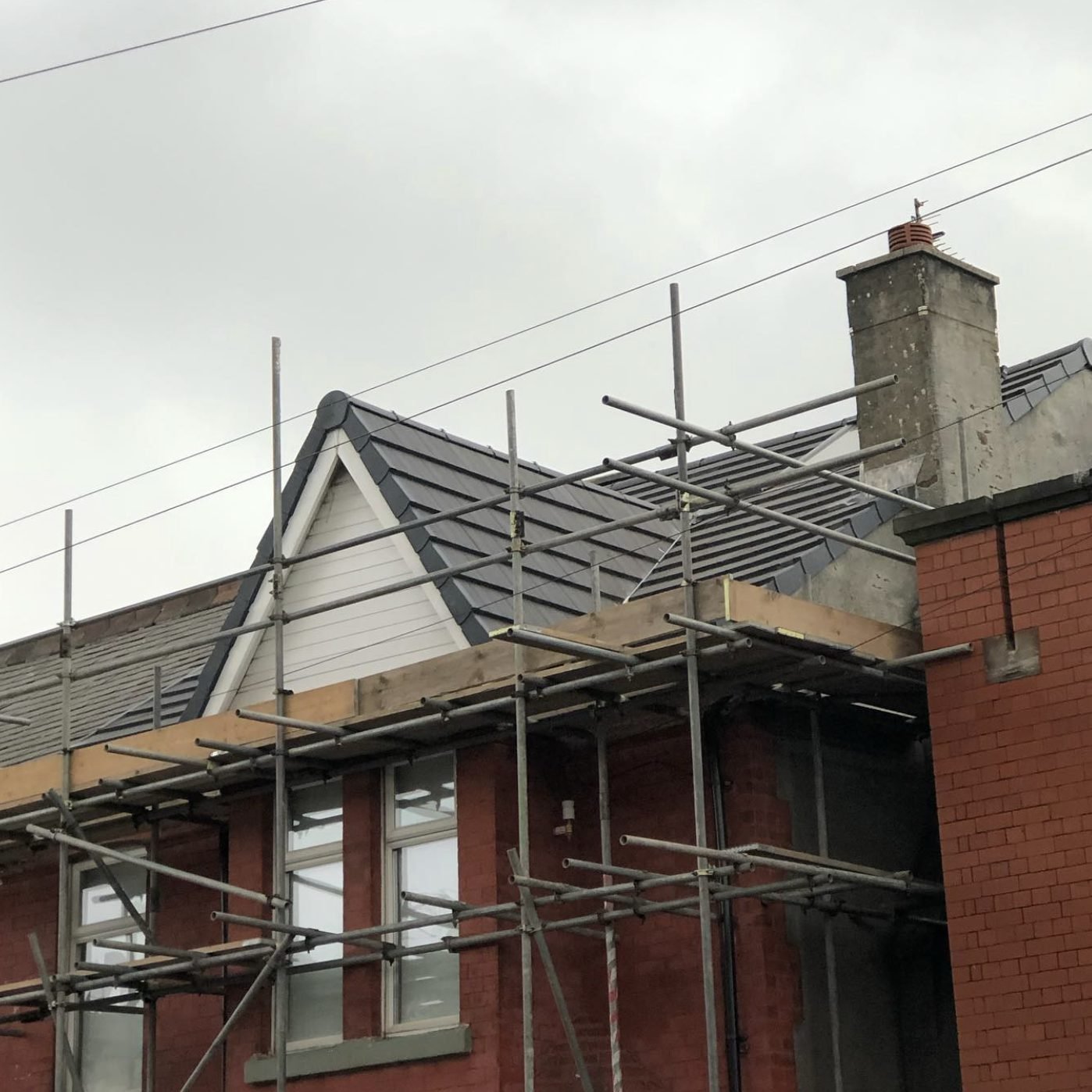Tiled gable dormer on a red-brick building, scaffold in front