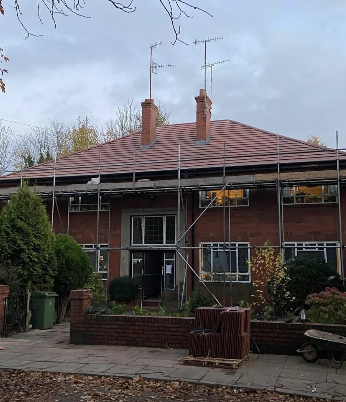 Brick house with a newly tiled red hipped roof, two chimneys and scaffold still up