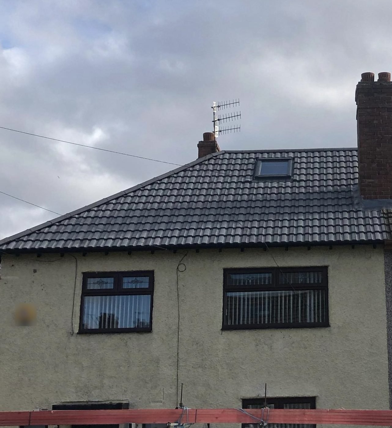 Hipped roof in dark interlocking tiles with a roof window and brick chimney