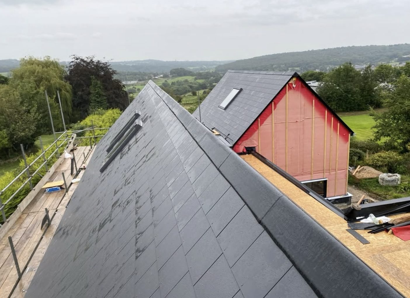 Newly slated roof with twin rooflights, scaffold alongside and open countryside beyond